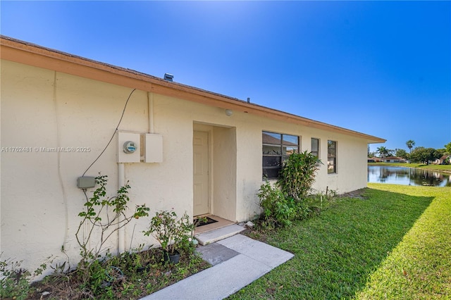 view of exterior entry featuring stucco siding, a lawn, and a water view