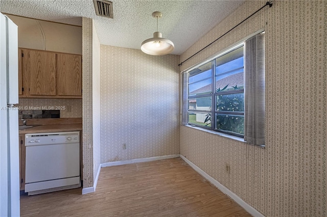 kitchen featuring light wood-type flooring, a textured ceiling, white dishwasher, and wallpapered walls