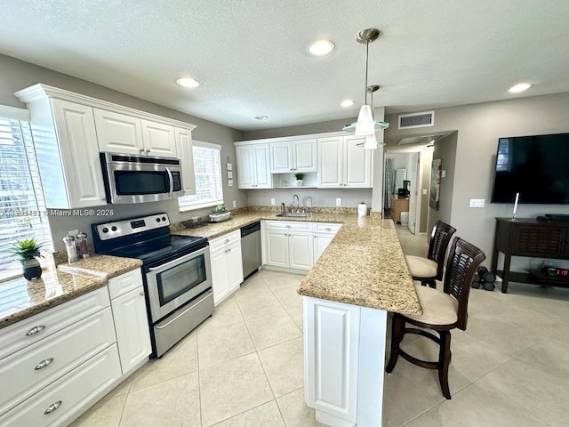 kitchen featuring visible vents, a breakfast bar area, a peninsula, stainless steel appliances, and a sink