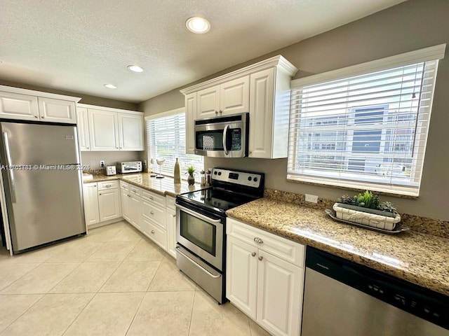 kitchen with light tile patterned floors, white cabinetry, stainless steel appliances, and a textured ceiling