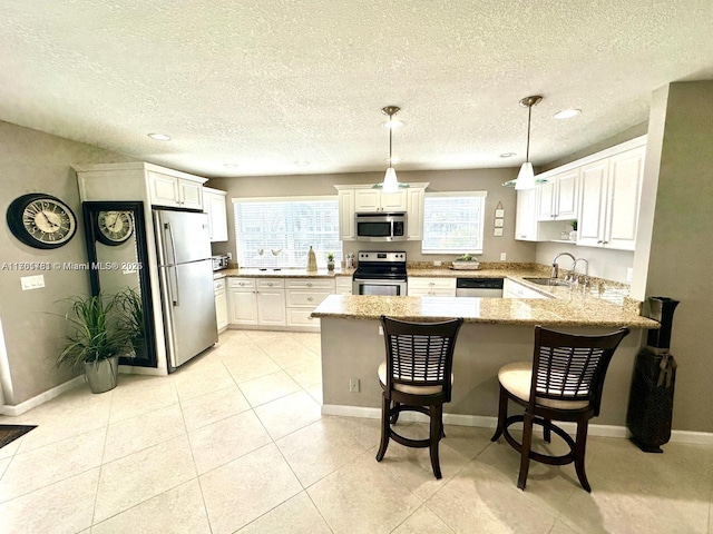 kitchen with light stone countertops, a peninsula, white cabinets, stainless steel appliances, and a sink