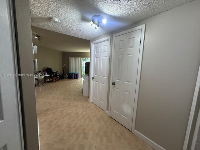 hall featuring light tile patterned floors, a textured ceiling, and baseboards