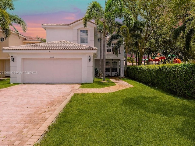 mediterranean / spanish house with a tiled roof, a front yard, stucco siding, decorative driveway, and an attached garage