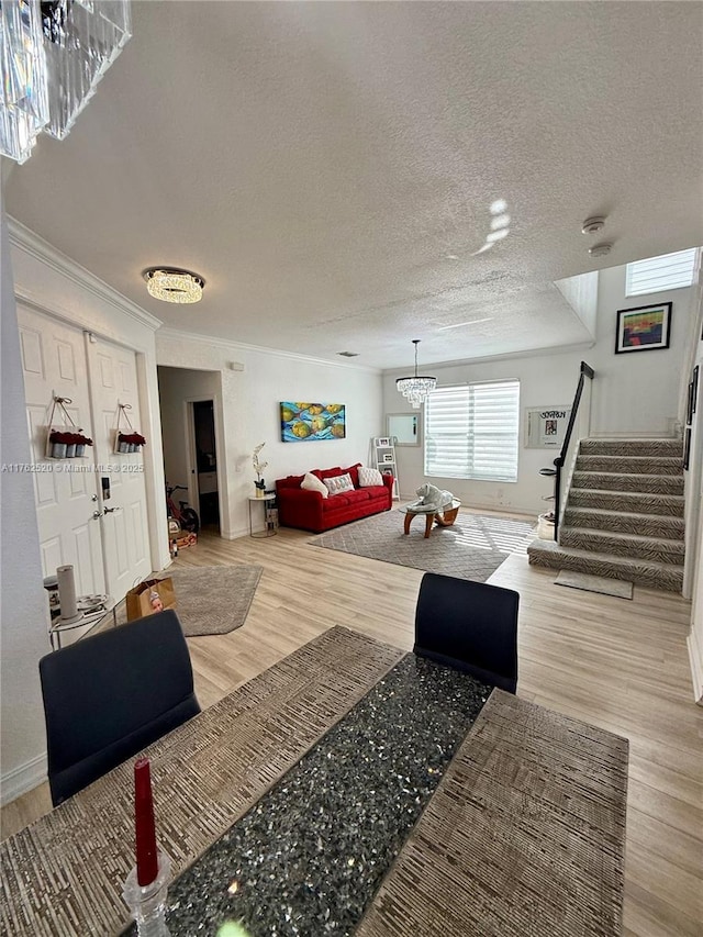 living room featuring ornamental molding, a textured ceiling, wood finished floors, stairway, and a chandelier