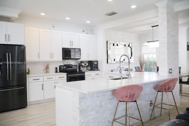 kitchen with freestanding refrigerator, a sink, white cabinets, range with electric stovetop, and a kitchen bar