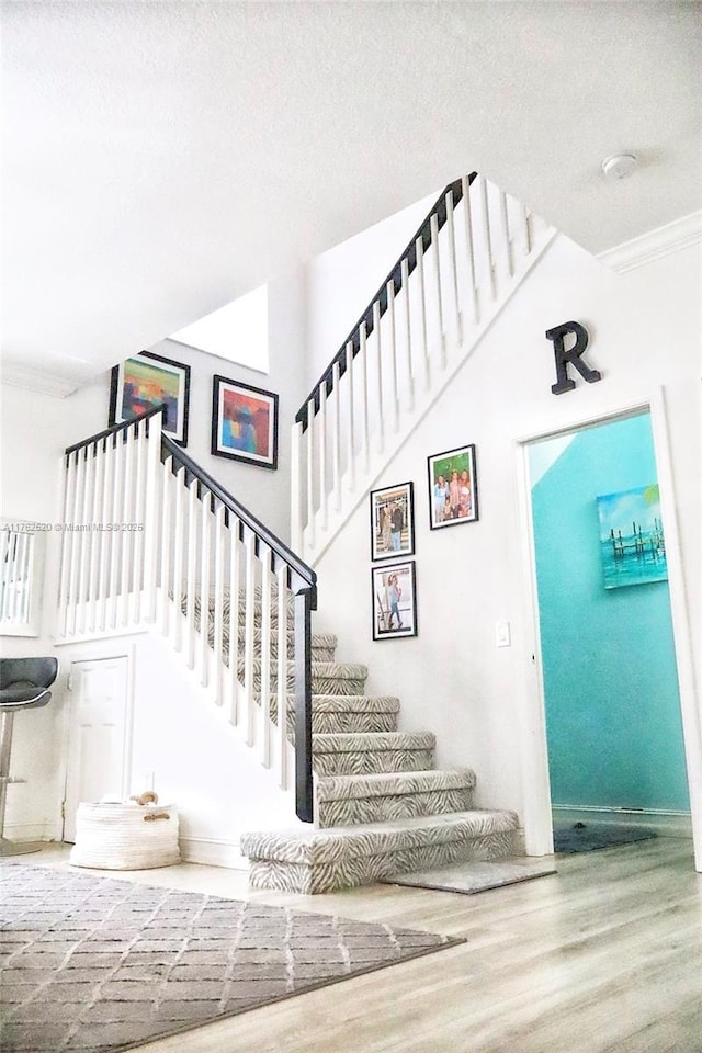 staircase with a textured ceiling, wood finished floors, and ornamental molding