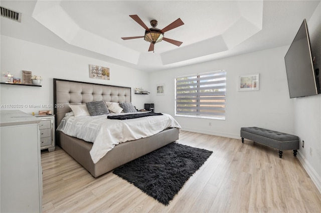 bedroom featuring light wood finished floors, visible vents, ceiling fan, baseboards, and a tray ceiling