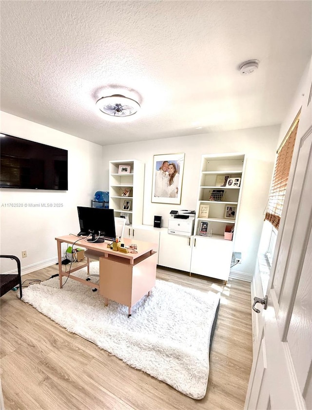 home office with built in features, baseboards, light wood finished floors, and a textured ceiling