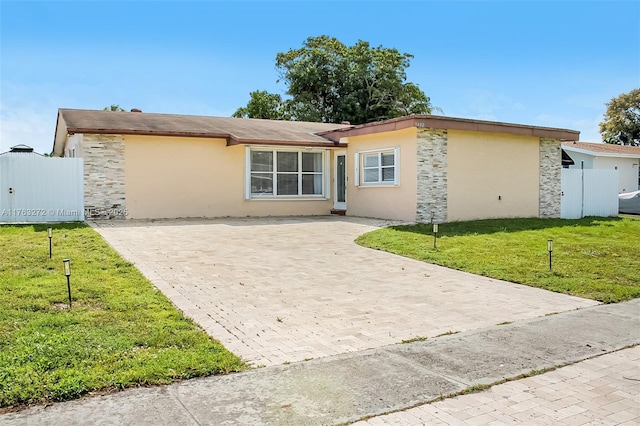 ranch-style home with a front lawn, fence, stucco siding, decorative driveway, and stone siding