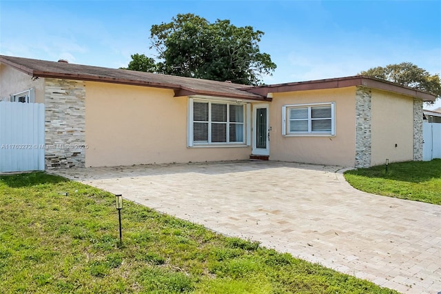 back of property featuring fence, stucco siding, a lawn, stone siding, and a patio