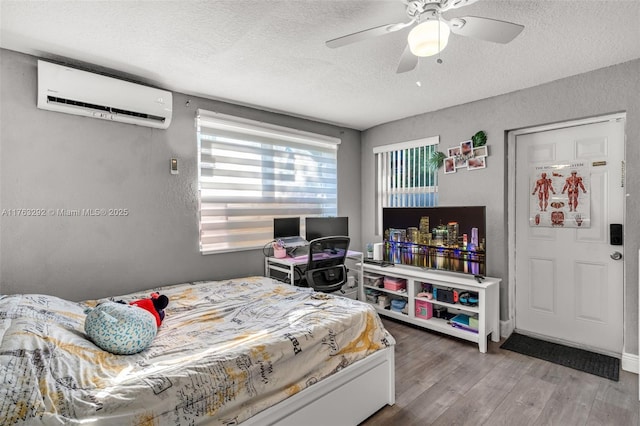 bedroom featuring ceiling fan, wood finished floors, a wall unit AC, a textured wall, and a textured ceiling