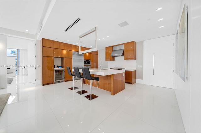 kitchen featuring visible vents, wine cooler, wall chimney exhaust hood, modern cabinets, and brown cabinets