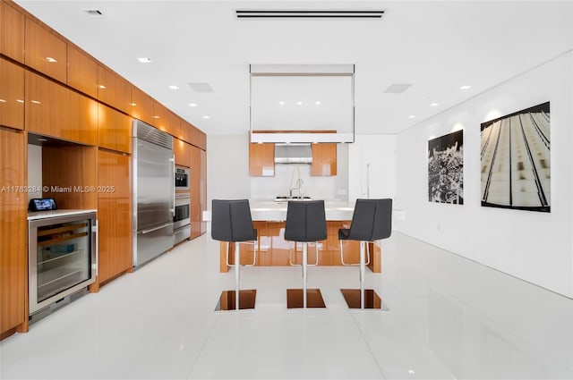 kitchen with modern cabinets, stainless steel built in refrigerator, beverage cooler, a kitchen breakfast bar, and light countertops