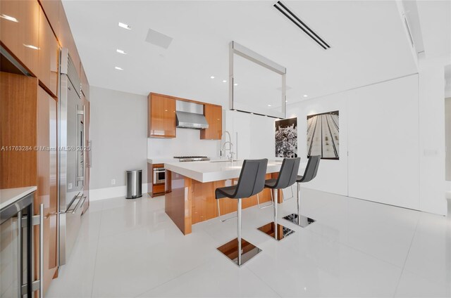 kitchen with visible vents, modern cabinets, a breakfast bar, wall chimney range hood, and light countertops