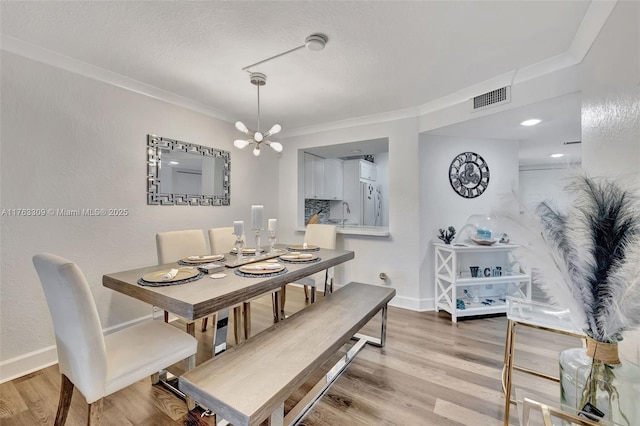 dining area with a notable chandelier, visible vents, crown molding, and light wood-type flooring