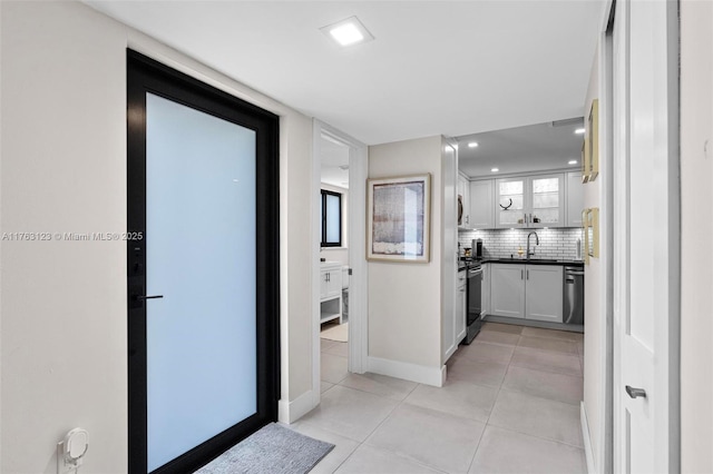 hallway featuring light tile patterned floors, recessed lighting, baseboards, and a sink