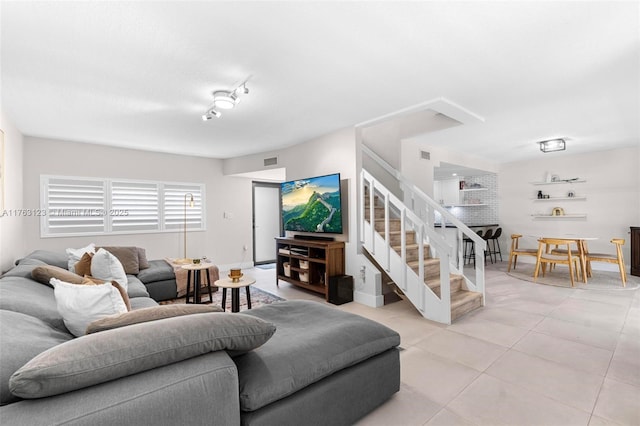 living area featuring light tile patterned floors, stairway, baseboards, and visible vents