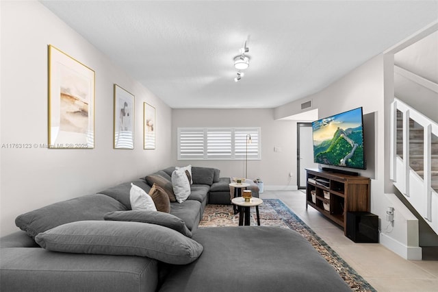 living room featuring light tile patterned floors, visible vents, baseboards, and stairs