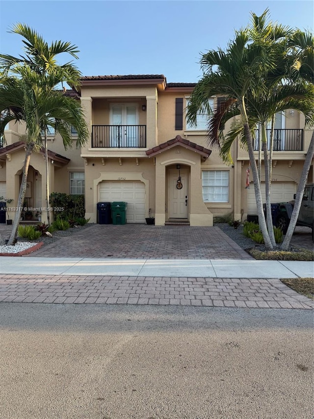 view of front of property with a tiled roof, stucco siding, decorative driveway, a balcony, and an attached garage