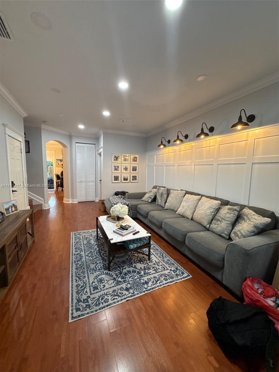 living area with visible vents, wood finished floors, recessed lighting, arched walkways, and crown molding