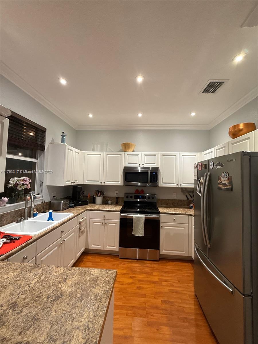 kitchen with light wood finished floors, visible vents, ornamental molding, stainless steel appliances, and a sink