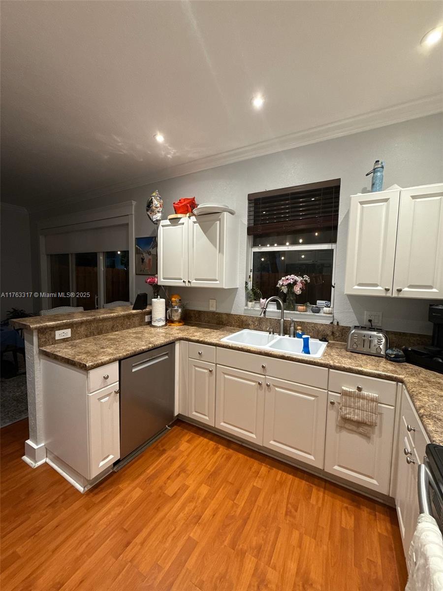 kitchen featuring stainless steel dishwasher, white cabinets, and a sink