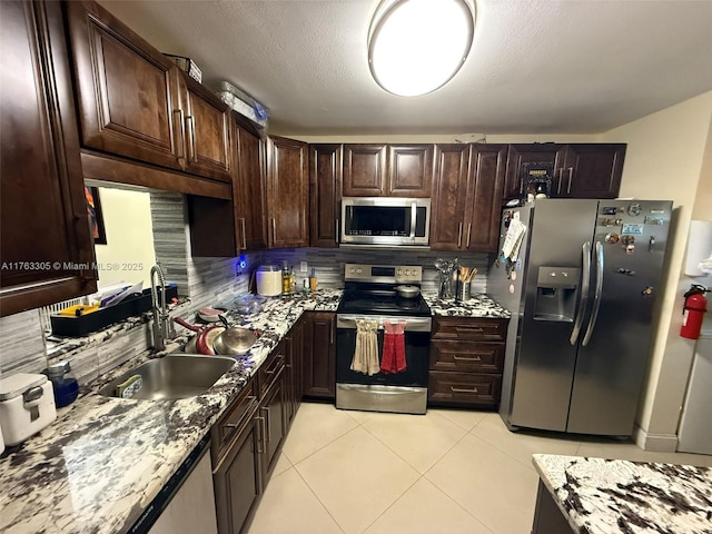 kitchen with a sink, stainless steel appliances, dark brown cabinetry, light tile patterned floors, and decorative backsplash