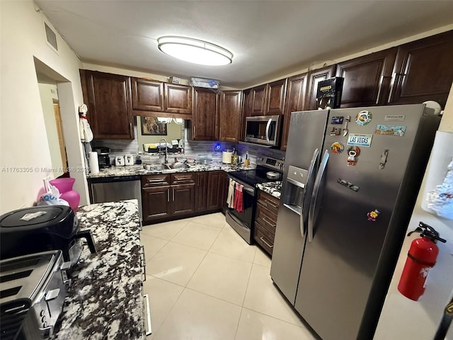 kitchen with tasteful backsplash, light stone countertops, dark brown cabinetry, light tile patterned flooring, and stainless steel appliances