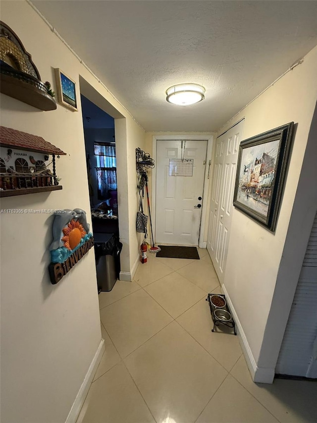 hall with light tile patterned floors, baseboards, and a textured ceiling