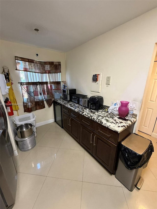 kitchen featuring light tile patterned floors, light stone countertops, baseboards, refrigerator, and dark brown cabinets