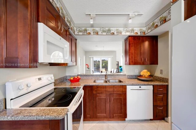 kitchen with a sink, white appliances, a textured ceiling, and light tile patterned floors