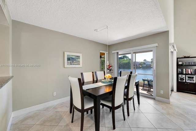 dining area with light tile patterned floors, a textured ceiling, baseboards, and a water view