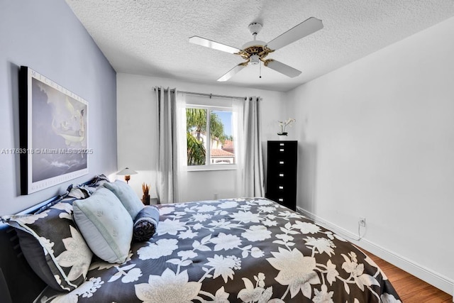 bedroom with ceiling fan, a textured ceiling, baseboards, and wood finished floors