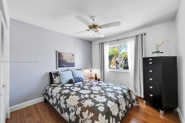 bedroom with a ceiling fan, wood finished floors, baseboards, and a textured ceiling