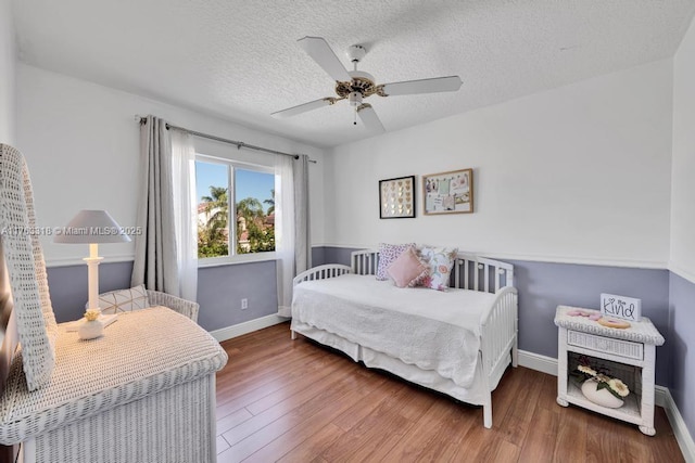 bedroom featuring ceiling fan, wood finished floors, baseboards, and a textured ceiling