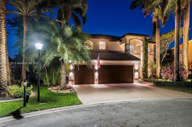 mediterranean / spanish-style house featuring decorative driveway, a tile roof, an attached garage, and stucco siding