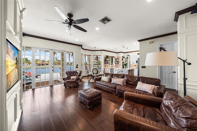living area with wood-type flooring, a ceiling fan, visible vents, and ornamental molding