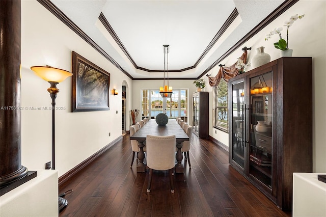 dining area featuring a raised ceiling, dark wood-type flooring, ornamental molding, arched walkways, and baseboards