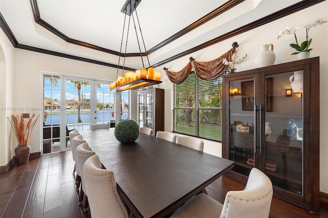 dining space featuring a water view, ornamental molding, french doors, a raised ceiling, and dark wood-style flooring