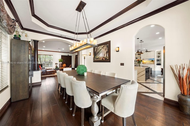 dining room featuring dark wood-type flooring, baseboards, a tray ceiling, arched walkways, and ornate columns