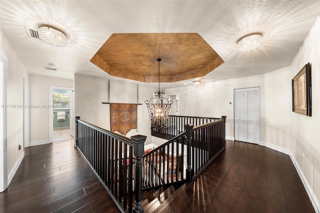 corridor featuring an upstairs landing, a chandelier, a tray ceiling, and hardwood / wood-style flooring