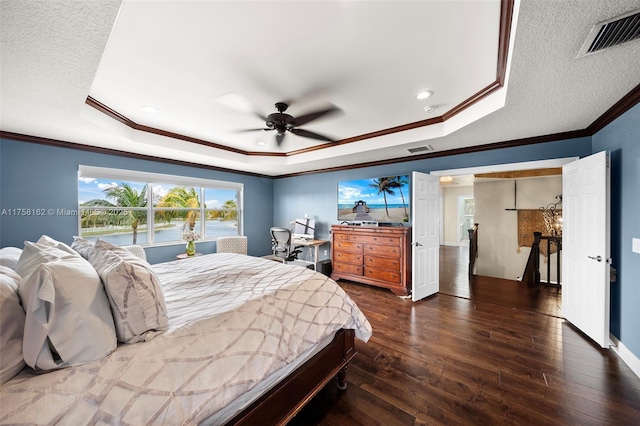 bedroom featuring visible vents, a tray ceiling, ornamental molding, dark wood-style floors, and a textured ceiling