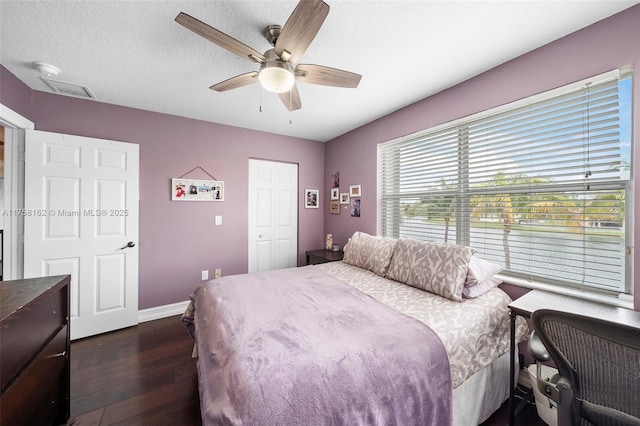 bedroom with ceiling fan, dark wood finished floors, baseboards, visible vents, and a closet