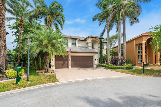 mediterranean / spanish-style house with stucco siding, driveway, a front yard, an attached garage, and a tiled roof