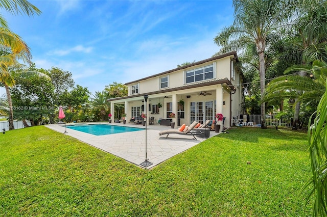 back of property with a yard, stucco siding, a ceiling fan, and fence