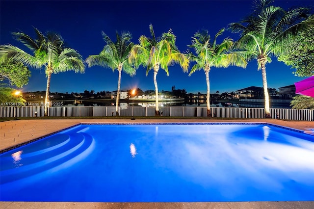 pool at night featuring a fenced in pool, a fenced backyard, and a water view