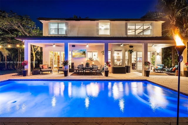 back of house at twilight featuring an outdoor pool, french doors, a ceiling fan, and a patio area