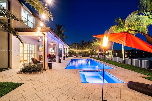 pool at night featuring fence, french doors, a fenced in pool, a patio area, and an in ground hot tub