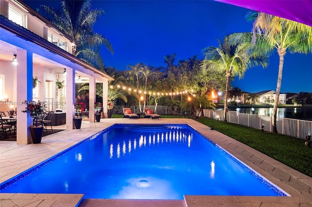 pool at night featuring a patio, a fenced backyard, a fenced in pool, and a water view