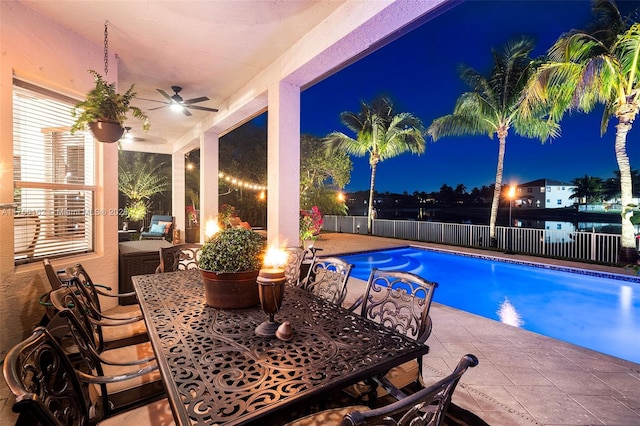 pool at night with a fenced in pool, a fenced backyard, a patio area, outdoor dining space, and a ceiling fan